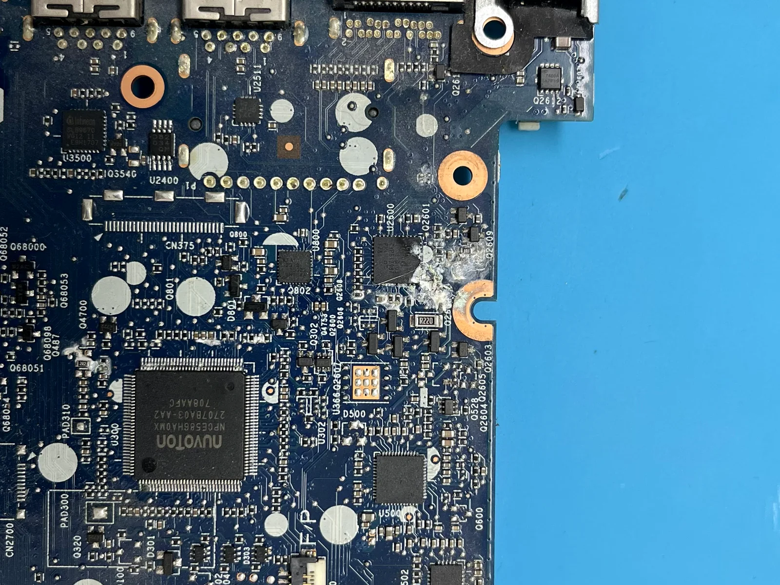 Placa madre de notebook con corrosión y residuos visibles junto a componentes electrónicos